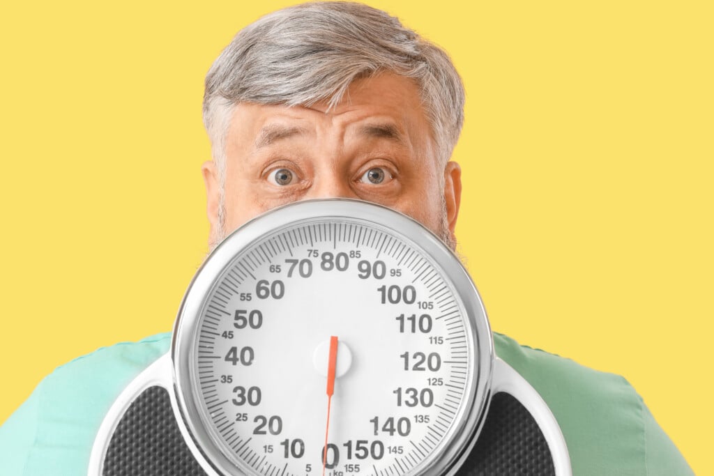 Overweight Shocked Mature Man With Scales On Yellow Background. Weight Loss Concept