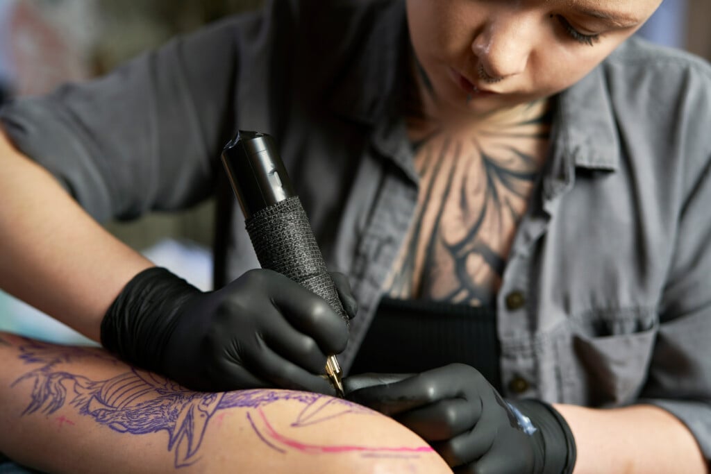 Close Up Of Tattoo Artist Drawing On Arm Of Client