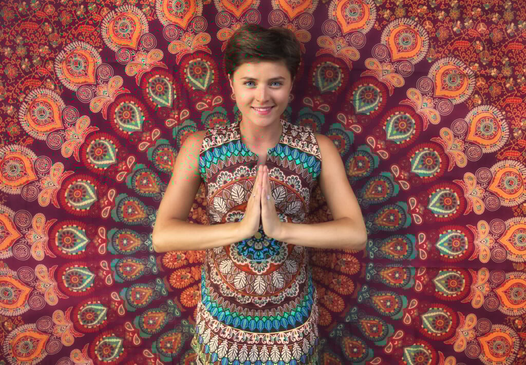 Namaste Greeting. Cheerful Young Woman On A Bright Background.