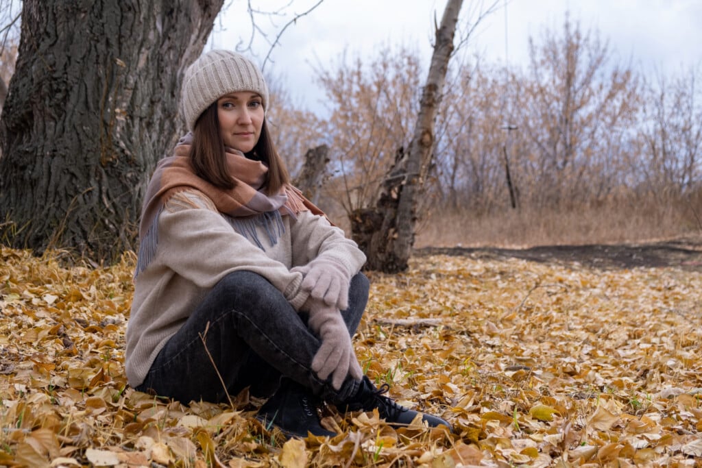 A Young Woman Sits On Autumn Foliage In The Park.