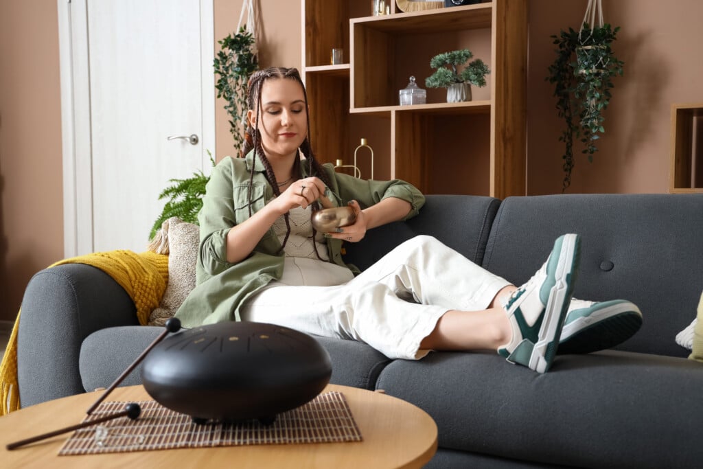 Young Woman With Tibetan Singing Bowl On Sofa At Home