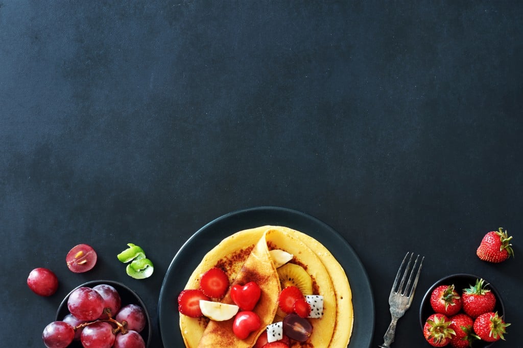 Top View Of Homemade Crepes With Strawberries, Grapes And Honey Over Black Background With A Copy Space.