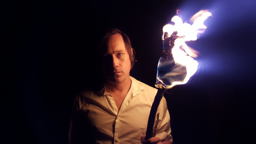 Adam Gnade stands with a lit torch lighting the photo