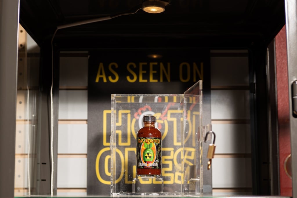 The millionth bottle of Da'Bomb sits in a clear box in front of a poster for the show Hot Ones