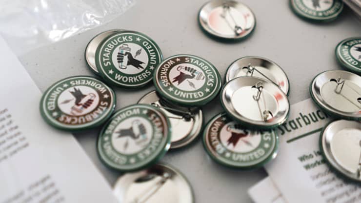 A collection of green Starbucks Workers United buttons are spread on a grey table on top of unionization paperwork