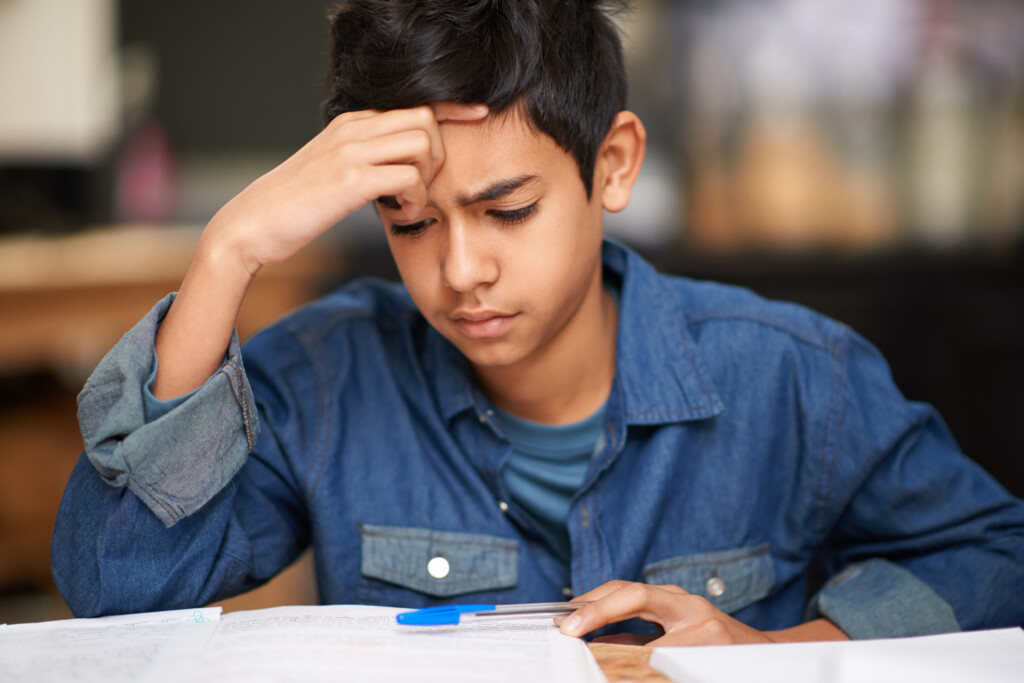 A young teenage boy frowns down at some school work