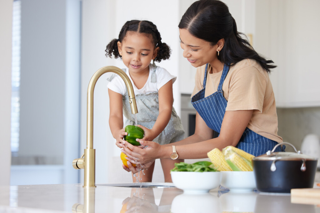mom and young child washing vegetables in kitchen sink