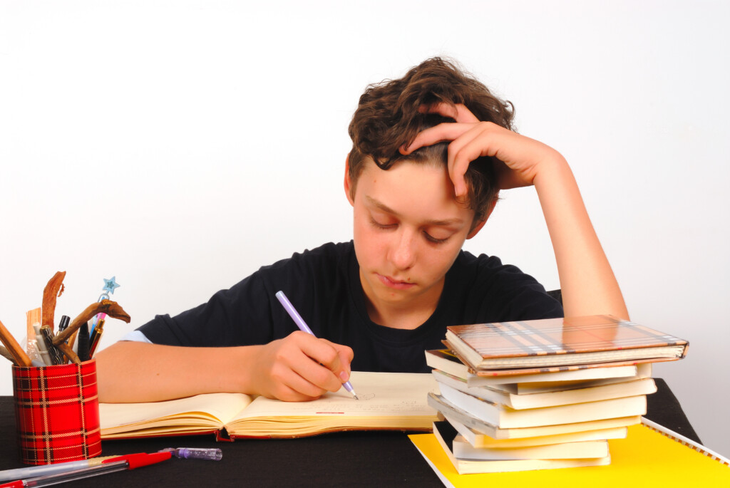 tween or teen boy doing homework, not looking very happy, for article on kids and homework