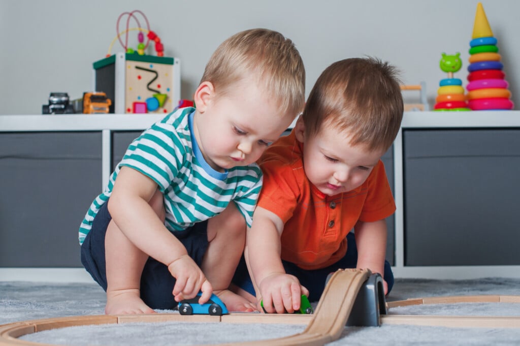 two toddlers playing together with wooden car track