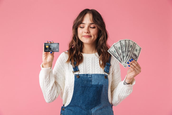 a girl holds cash in one hand and a credit card in the other, for article on teens and money management