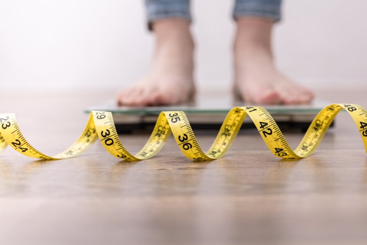 Female Leg Stepping On Weigh Scales With Measuring Tape, for article on eating disorders