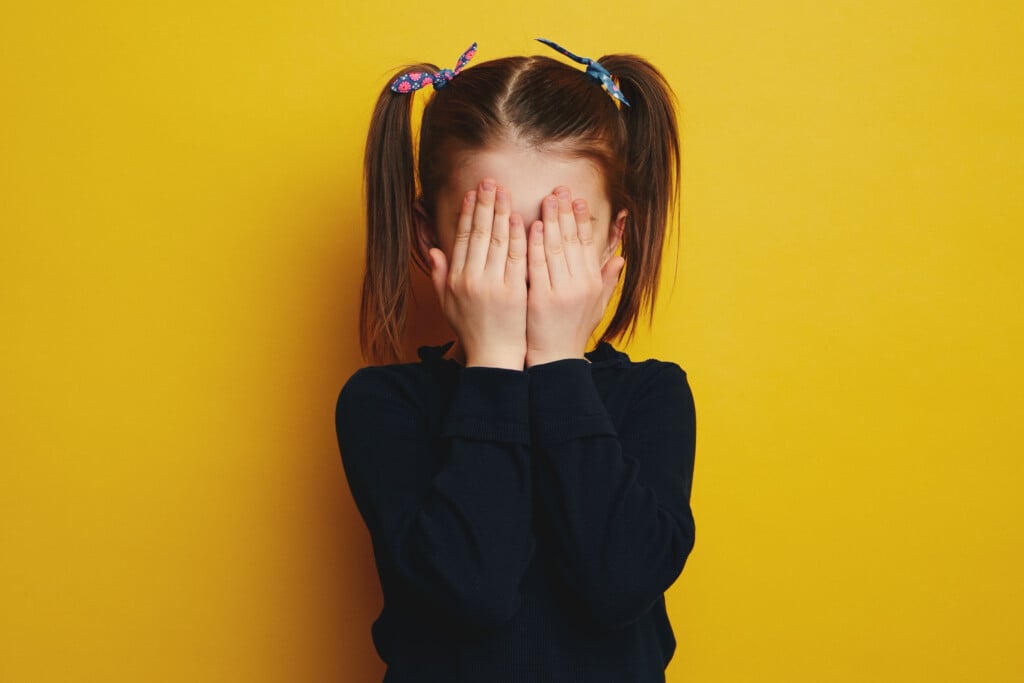 young girl with hands over her face, experiencing social anxiety