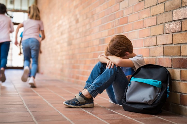 young boy sits on ground with head in hands, for article on dealing with bullies