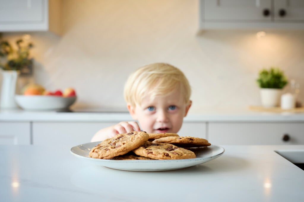 young boy sneaking a cookie from a plate of cookies, possibly displaying a lack of self-control