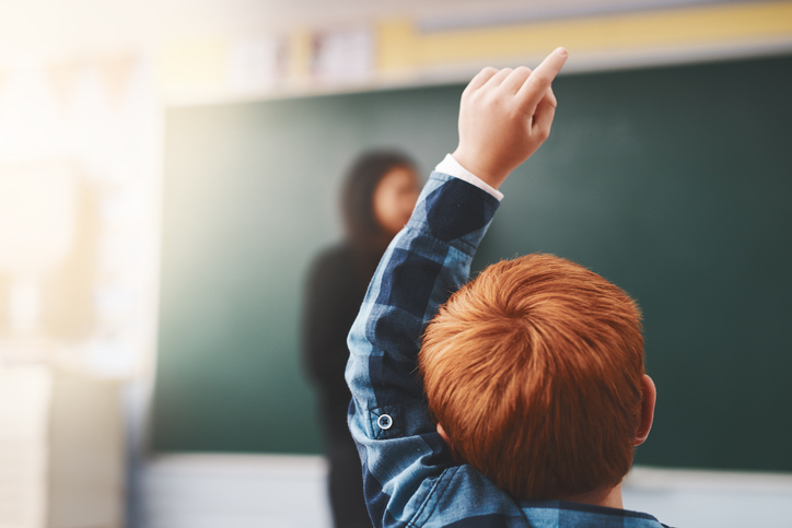 red haired boy raising hand in class, for article on public schools debate