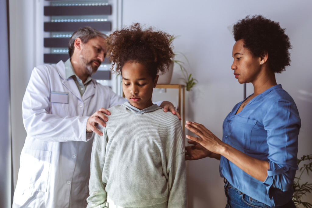 doctor and parent looking at girl's back, for article on scoliosis