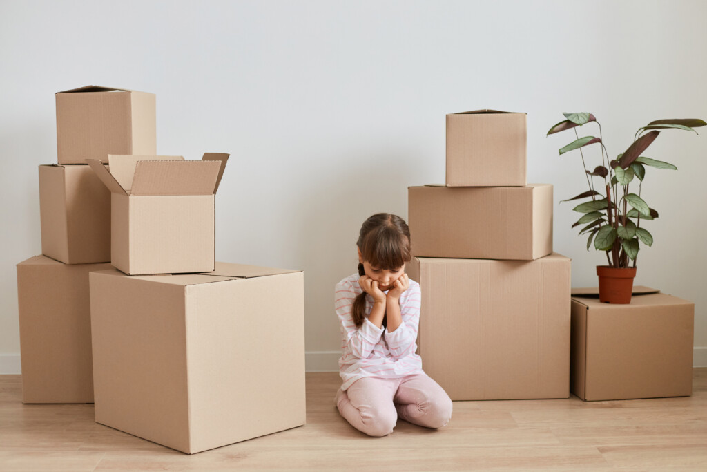 sad girl surrounded by moving boxes, for article on helping kids adjust to a move