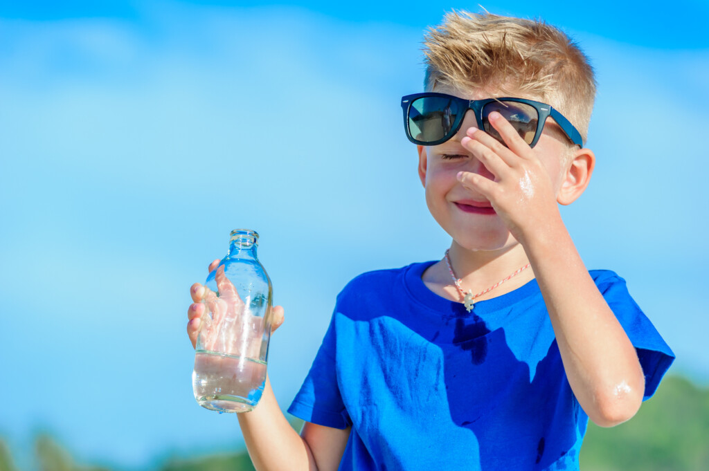 young boy with water bottle looking too hot, for article on heat-related illness