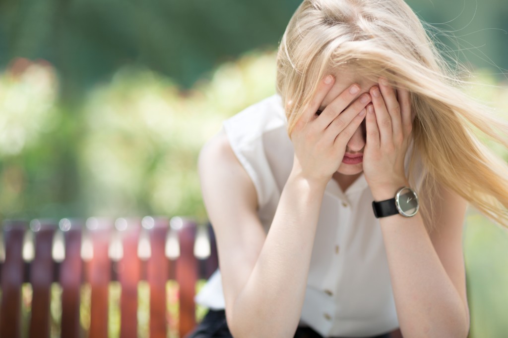tired and sad woman sitting on bench with head in hands, for article on parenting fatigue