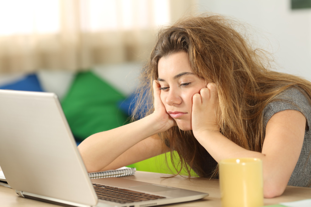 a tired teen sits at a computer. for article on teens and sleep