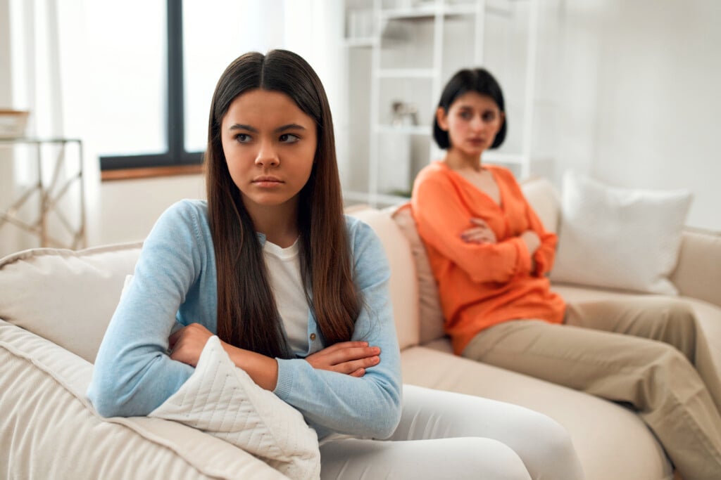 angry teenage daughter on couch with mother in background