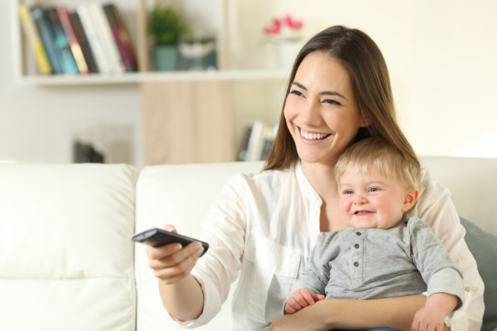 mother holding baby and remote, for article on secondhand tv