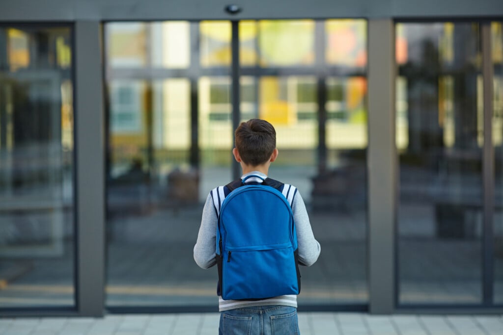 student with backpack standing in front of school door