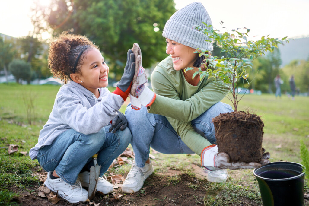 a child and woman high five as they plant a tree, for an article on volunteering with your kids