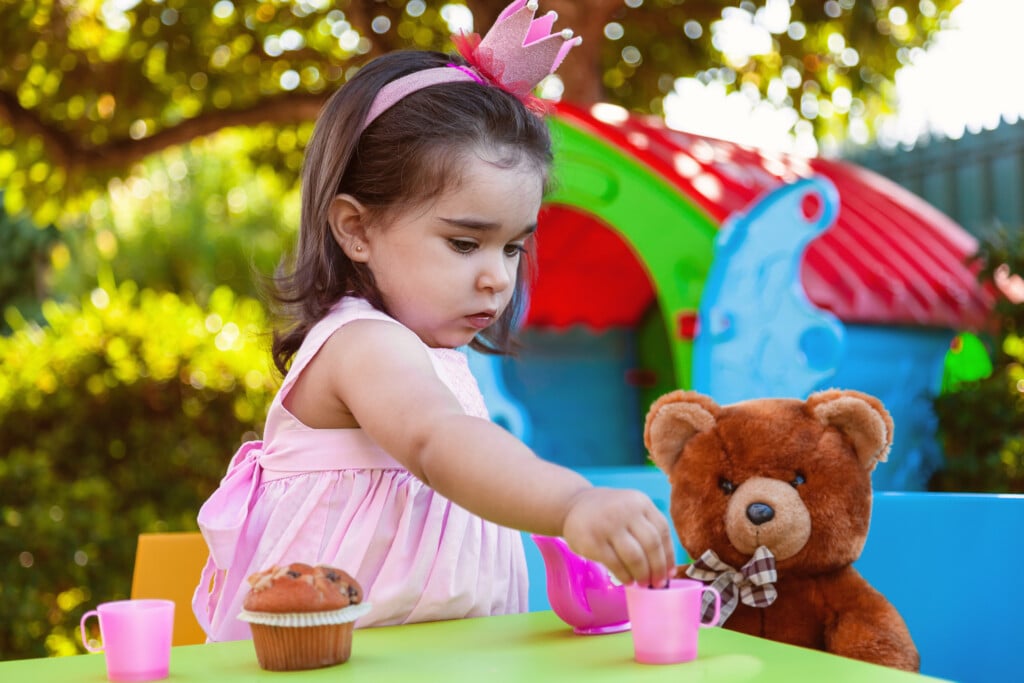 toddler girl having a tea party with a teddy bear