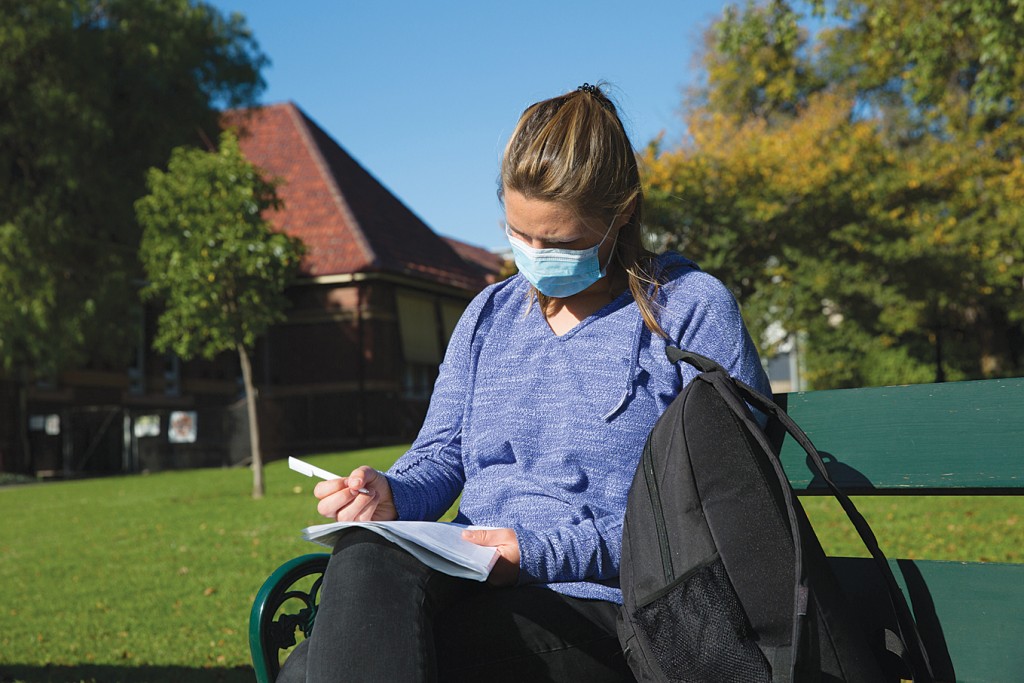 college student studying outside wearing face mask, for article on college and covid-19