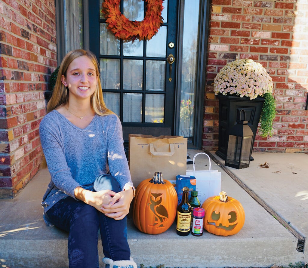 Delaney Ferguson sitting on a porch with carved pumpkins