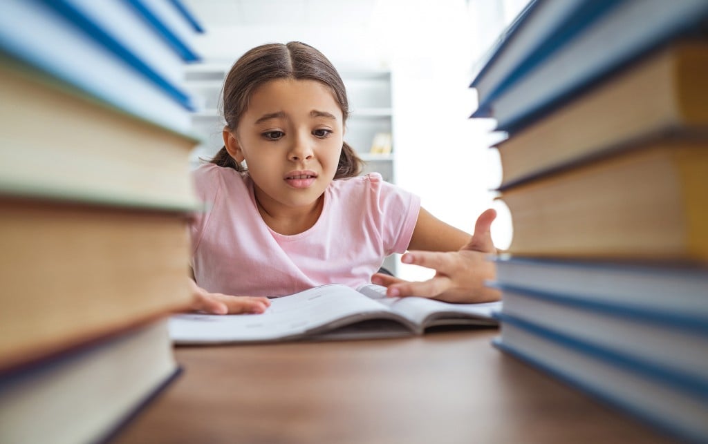 girl surrounded by books looking stressed, for article on helping kids manage stress