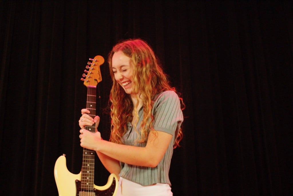 Sophie Raskin holds an electric guitar and smiles