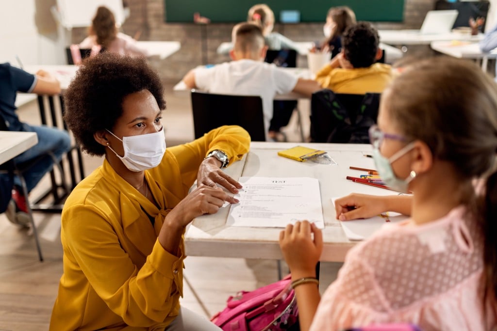 teacher with face mask talks to student, for article on reopening schools