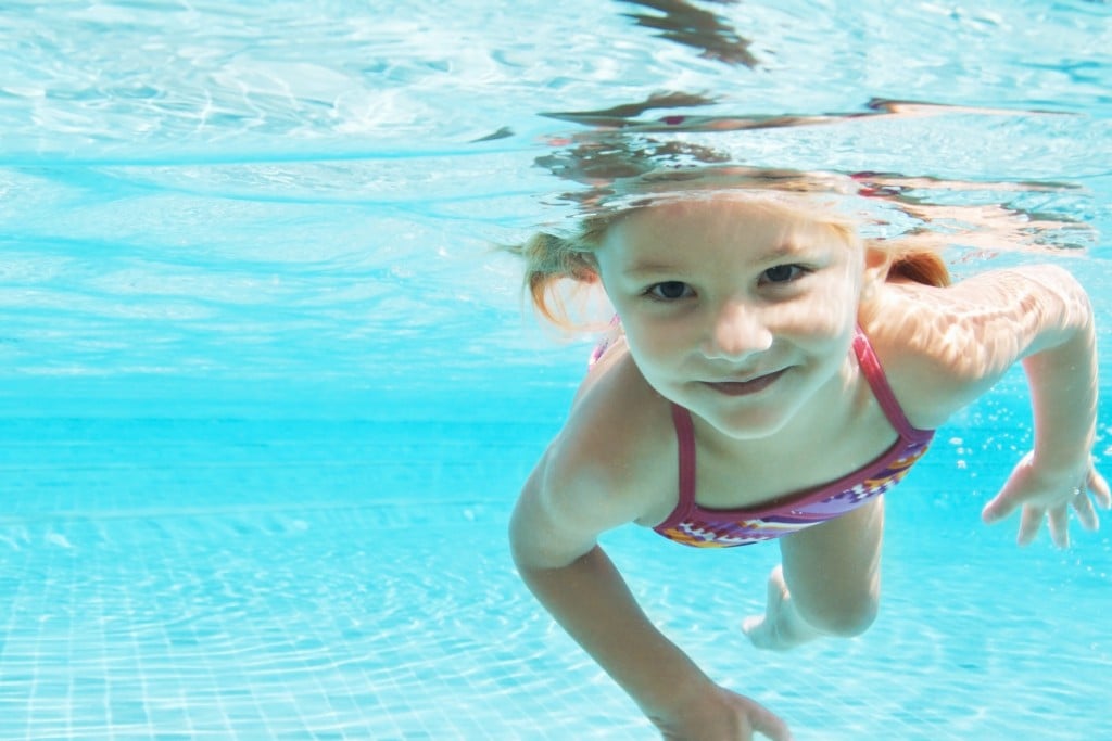 smiling girl swimming underwater, for article on summer camp safety