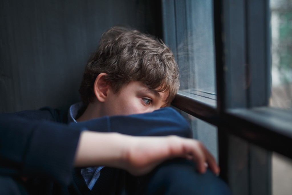 sad teen boy at window, for article on male eating disorders