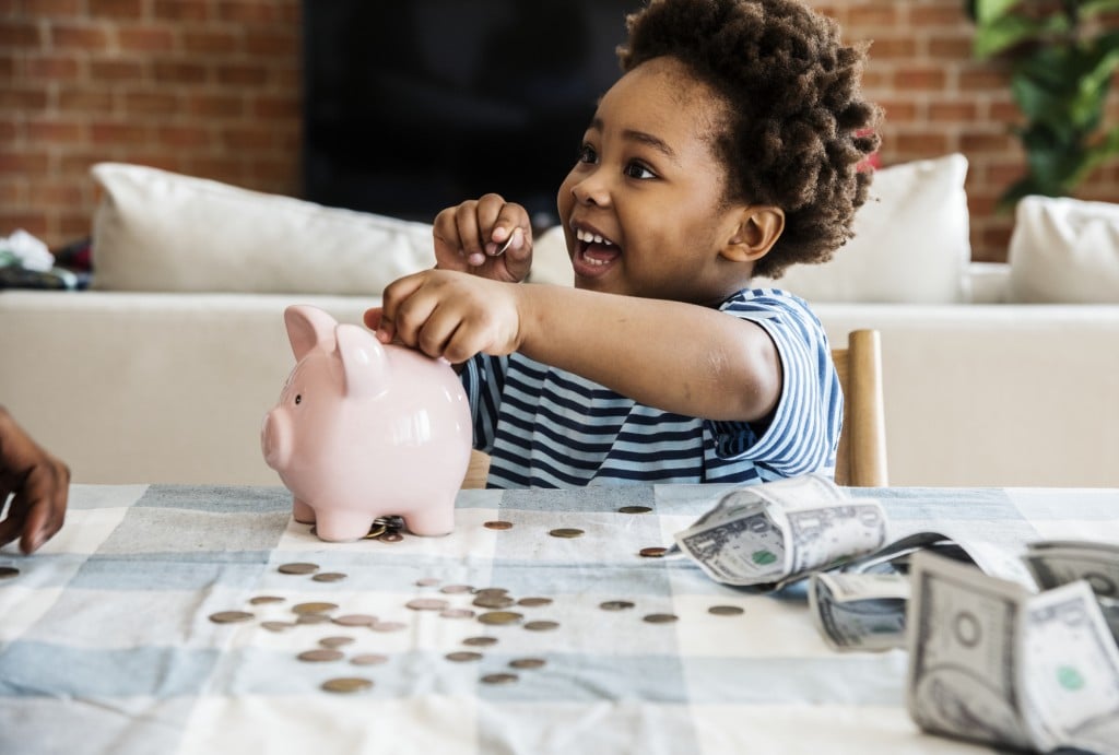 young boy putting money in piggy bank, for article on the american rescue plan