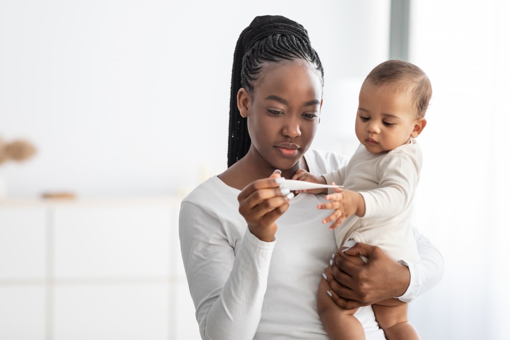 Happy Young African American Mother Looking At Thermometer