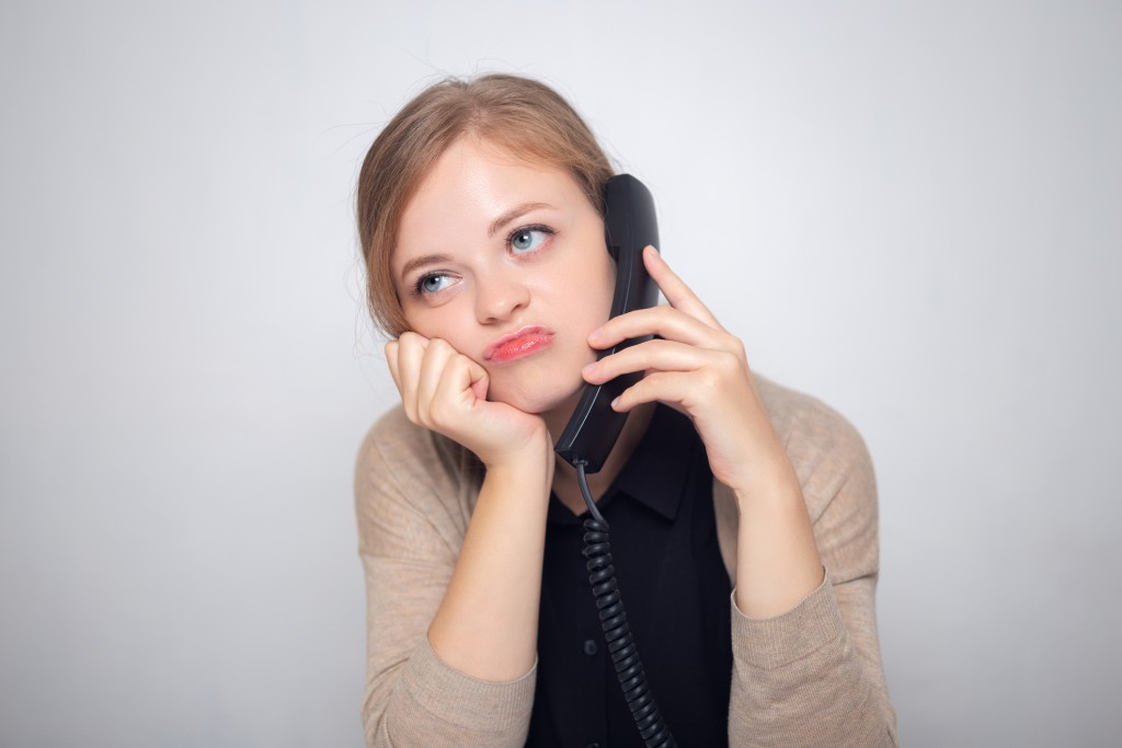 Young Caucasian Woman Is Talking On The Landline Phone, Bored, Tired Or Annoyed