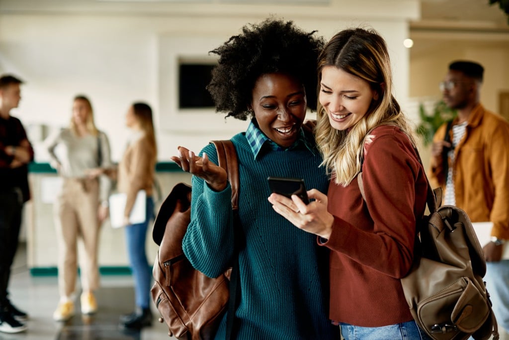 two college age female students looking at smart phone and smiling. college prep apps concept