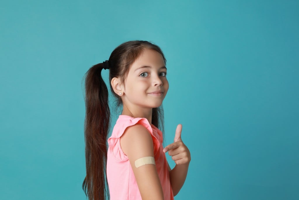 girl points to vaccine bandaid. for an article on covid-19 vaccines for kids