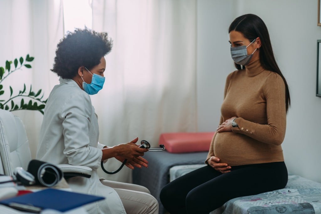 doctor and pregnant woman both wearing masks, for article on pregnancy and covid