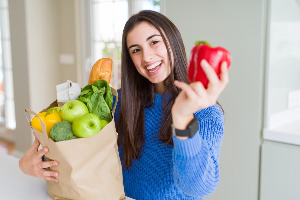 Young Beautiful Woman Smiling Holding A Paper Bag Full Of Groceries At Home