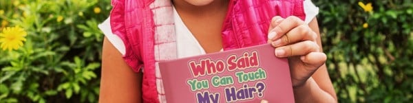 Young girl holds book titled Who Said You Can Touch My Hair?