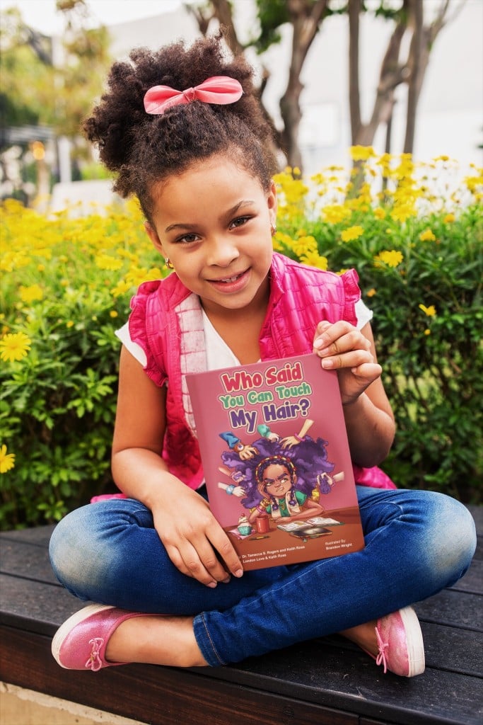 Young girl holds book titled Who Said You Can Touch My Hair?