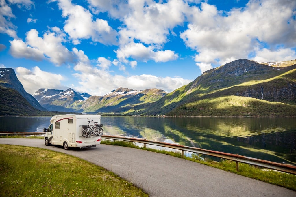 RV driving on road next to lake and mountains