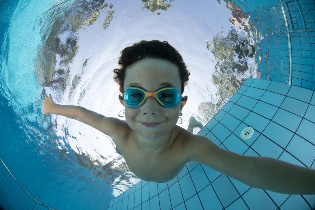 young boy swimming underwater with goggles
