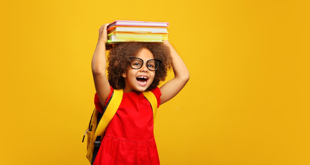 Funny Smiling Child School Girl With Glasses Holding Books On Her Head