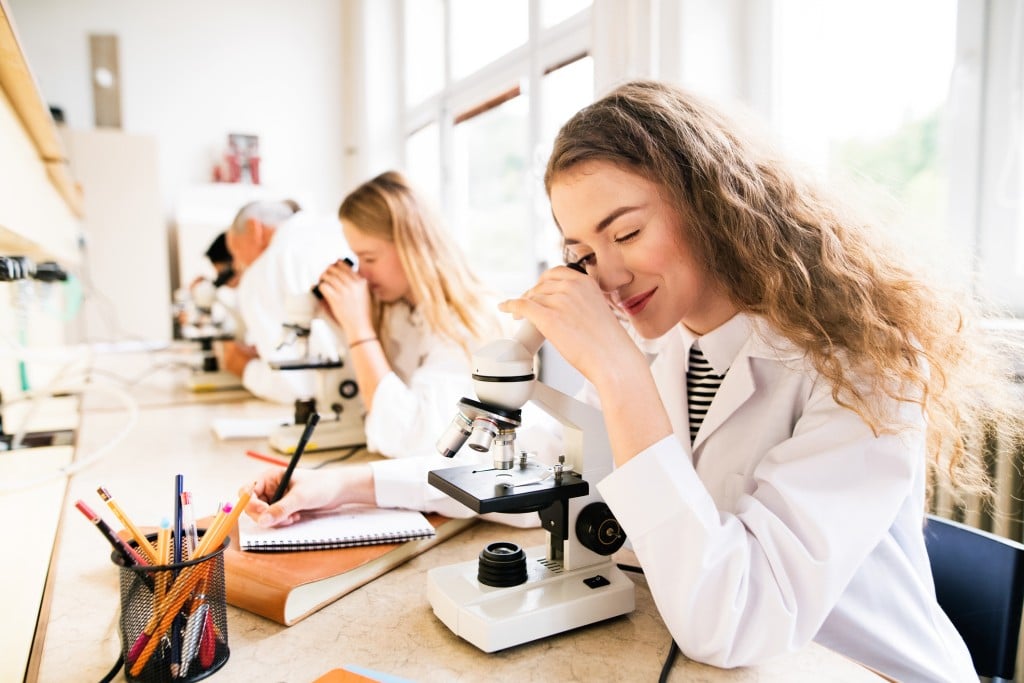 Beautiful High School Students With Microscopes In Laboratory.