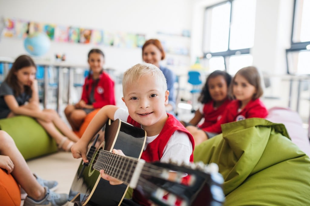 A boy with down syndrome With School Kids And Teacher Sitting In Class, Playing Guitar, for article on iep services